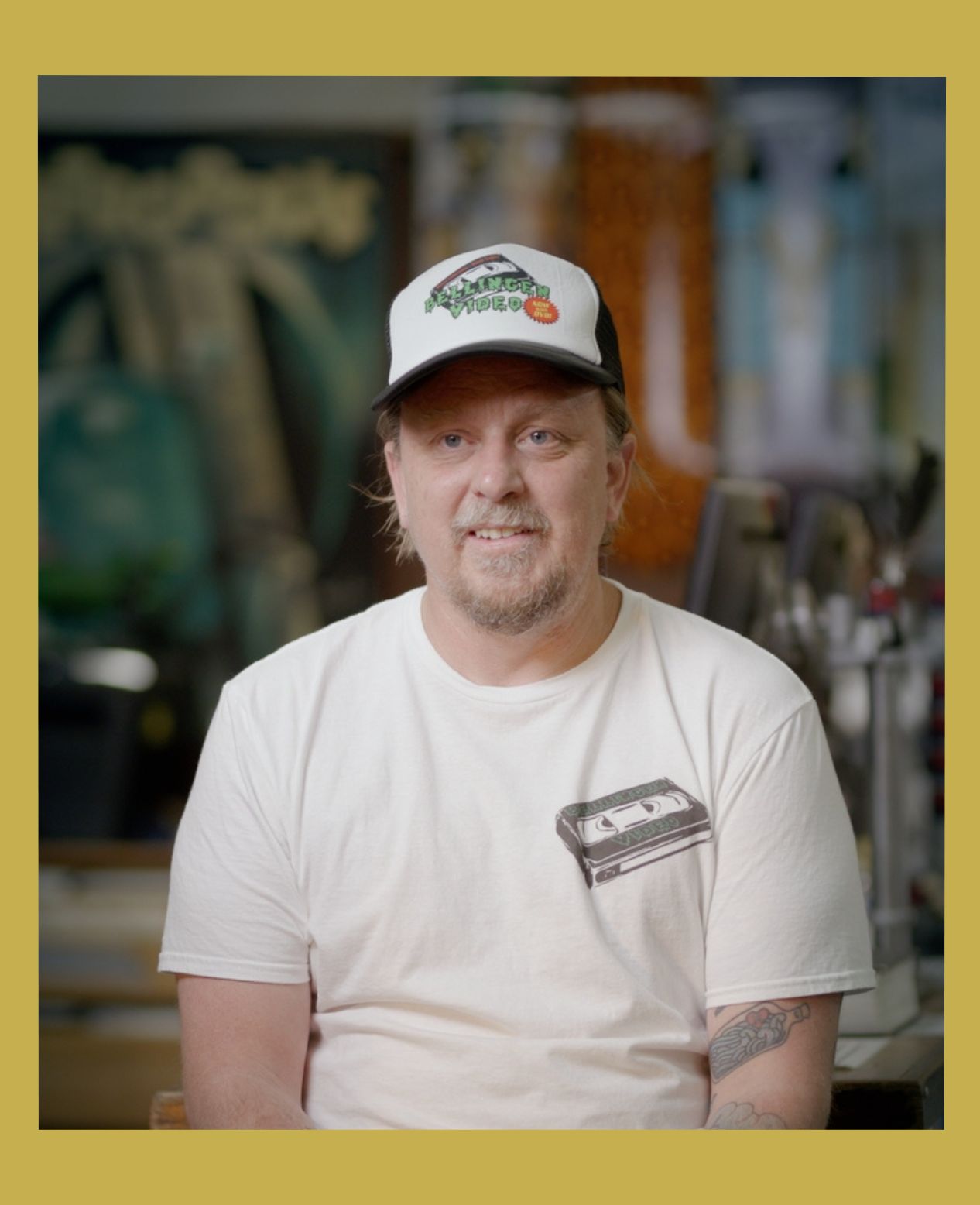 Image has a gold border and is of Rod O'Hara owner of Bellingen Video Connection in his store looking at camera in the documentary Return Chute: The survival of a small town video store