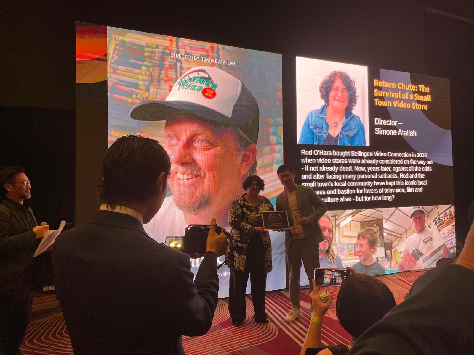 Documentary Return Chute: The Survival of a small town video store director and producer Simone Atallah stands in front of a large screen to receive the Special Jury Award at the Sydfest Independent FIlm Festival 2024.