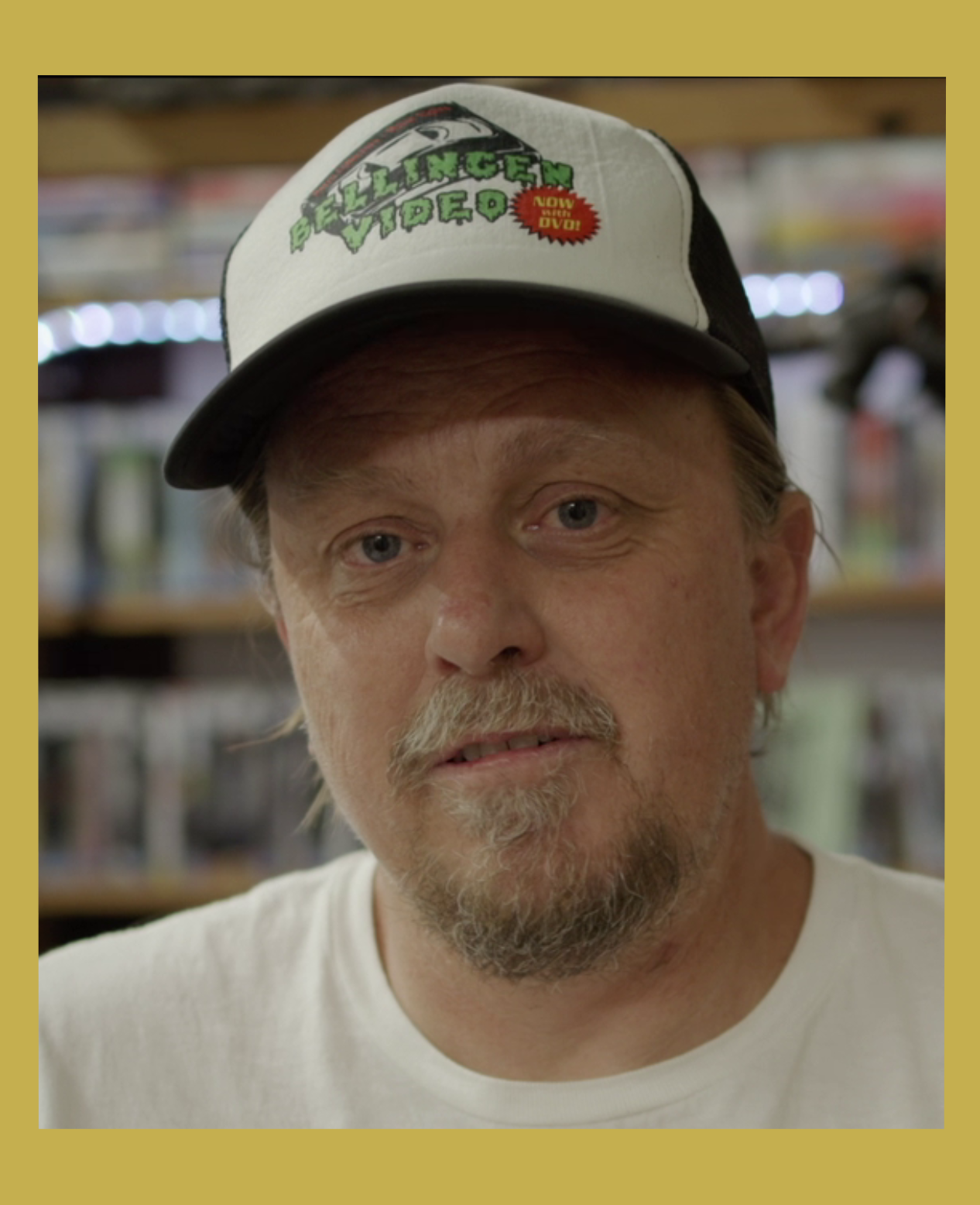 Image has a gold border and is of Rod O'Hara owner of Bellingen Video Connection in his store looking at camera in the documentary Return Chute: The survival of a small town video store